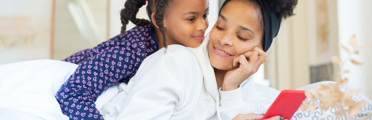 Mom and daughter lie in bed and check a mobile phone together